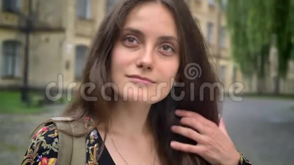 年轻漂亮的女人留着长发站在街边看着摄像机学生观念视频的预览图