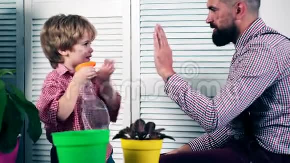 一个男孩和他的父亲拍手给花浇水父子俩在花盆里种花的概念视频的预览图