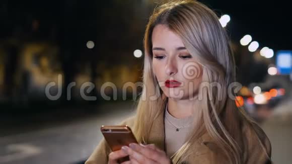 迷人的女人在夜城街头散步时使用智能手机女孩叫出租车在线服务出租车订单视频的预览图