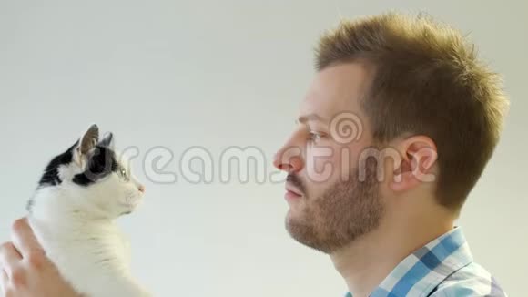 时尚的年轻白种人带着一只猫到他的脸上看着她特写白色背景发型视频的预览图