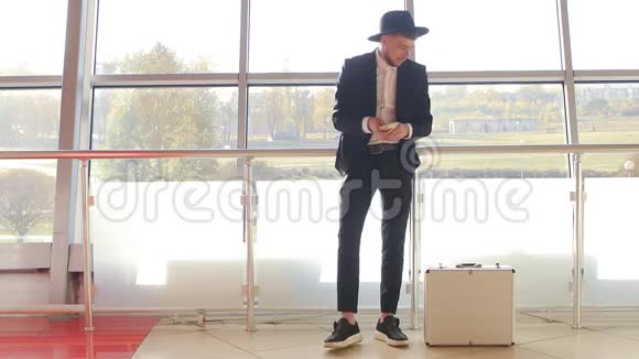 一个穿着帽子和黑色西装的时髦男人在银行里把钱放在手提箱里慢着更富有视频的预览图