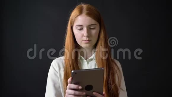 红姜女将平板电脑屏幕用焦糖制成相机隔离在黑色背景上视频的预览图