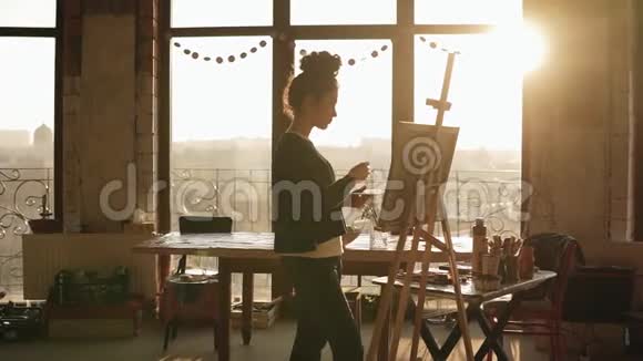 完全集中的老练的女艺术家在她20的画架上画着画后面的太阳照亮了艺术视频的预览图
