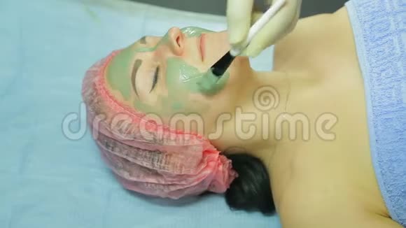 美容师在一个女人的脸上涂上一层灰色粘土的化妆面具视频的预览图