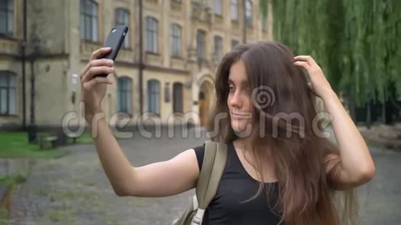 年轻迷人的女学生留着长发自拍在大学里站在公园里快乐快乐视频的预览图