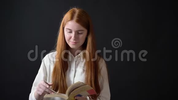 可爱的少女带着姜发看书看着相机站在黑色的背景上视频的预览图