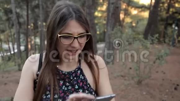 一个年轻的女孩走在森林里在手机上寻找网络找到了一个朋友视频的预览图