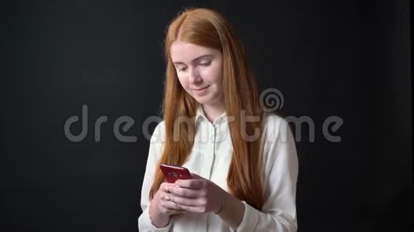 穿着白色衬衫的年轻姜女在电话里发短信摸着她的头发被隔离在黑色的背景上视频的预览图