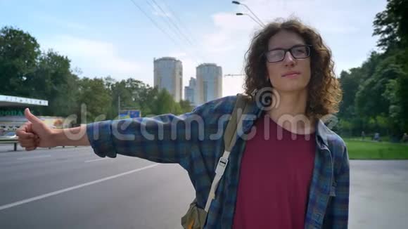 戴眼镜的年轻人一头长长的波浪发举起手等待出租车向前看站在路边视频的预览图