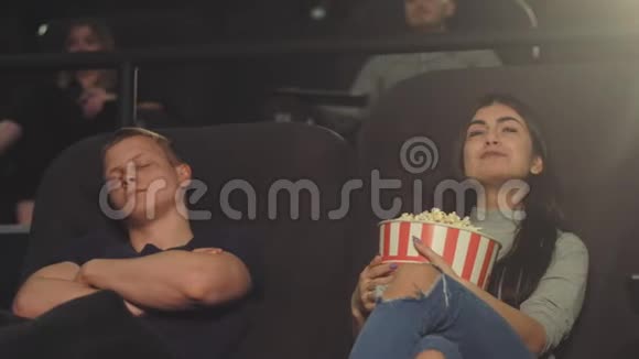 一个年轻人在电影院里看电影时睡着了而他的女孩则热情地继续看电影视频的预览图