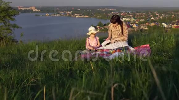 妈妈和女儿正在画坐在湖边的一座小山上视频的预览图