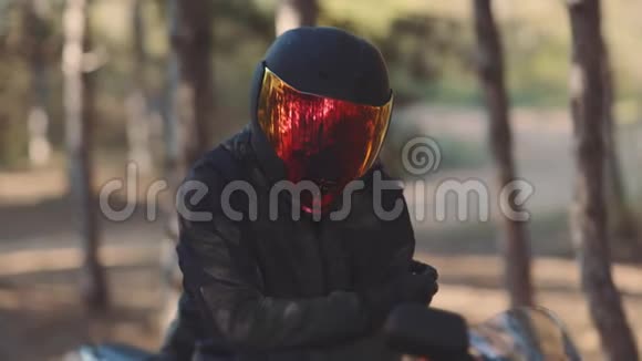 日落时戴黑色头盔的摩托车手的肖像森林中的自行车彩色面罩视频的预览图