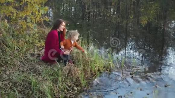 母亲和孩子坐着在湖边聊天拥抱着秋天的风景视频的预览图