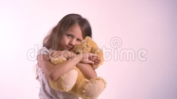 小可爱的女孩拥抱她的毛绒玩具熊孩子拥抱玩具孤立地站在明亮的粉红色工作室背景上视频的预览图