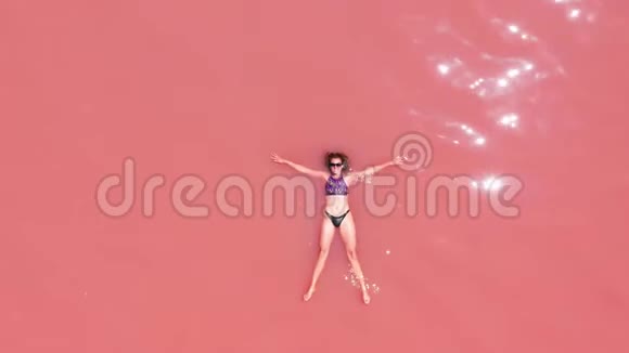 空中观景一个美丽的年轻女孩躺在粉红色的湖里一件比基尼太阳镜粉红色的清澈的水一张最高的风景视频的预览图