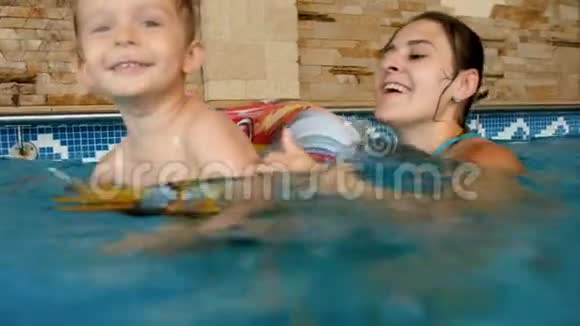 3岁小男孩带着充气的彩色戒指在室内游泳池游泳的4k视频视频的预览图