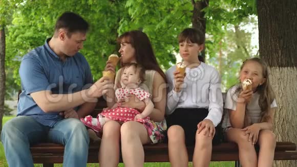 有父母的孩子坐在公园里的长凳上吃冰淇淋笑幸福家庭视频的预览图