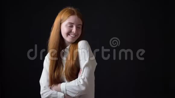 害羞迷人的女人长着一头姜黄色的长发穿着白色衬衫对着镜头微笑被隔离在黑色背景上视频的预览图