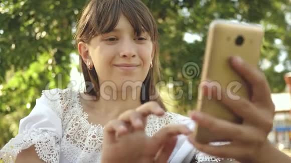 年轻女孩在平板电脑上和朋友聊天美丽的女孩在智能手机上写一封信在春天夏天公园里视频的预览图