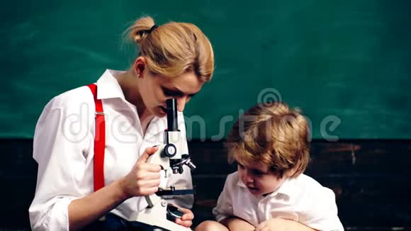 年轻的女人带着一个小男孩在绿色的木板背景上的显微镜里看着一个小麦茎教师和学生视频的预览图