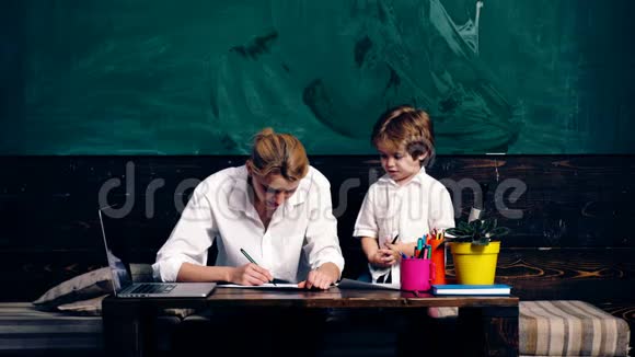 一位带着一个小男孩的老师在桌子上的笔记本上做笔记背景是学校董事会在视频的预览图