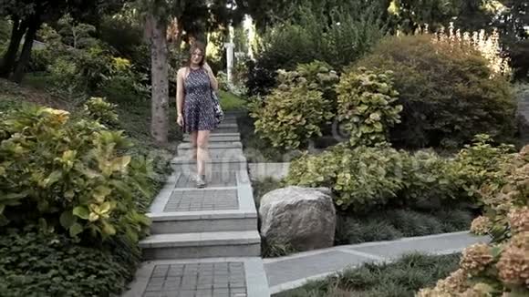 一个年轻的女孩走下美丽的台阶这台阶位于一个有各种奇花异草和树木的绿色公园里视频的预览图