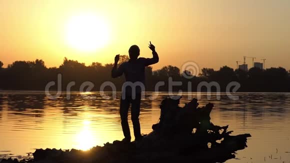 戴着耳机跳舞的年轻人在太阳落山时举手视频的预览图