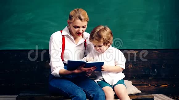 老师带着一个小男孩在教室里的绿色黑板的背景下在笔记本上写作学习概念视频的预览图