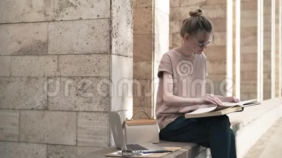 有魅力的年轻女人坐在外面看书石头建筑侧视视频的预览图