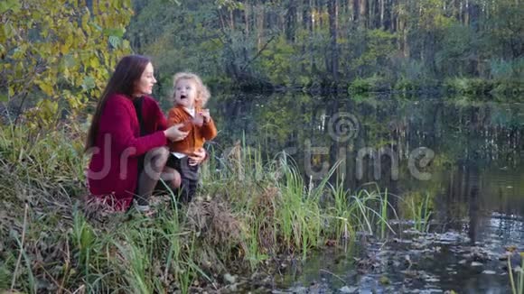 母亲和孩子坐着在湖边聊天拥抱着秋天的风景视频的预览图