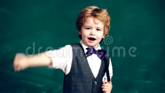 一个小男孩手里拿着一支笔然后把它藏在绿色学生板的背景上视频的预览图