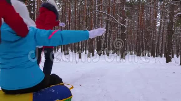 孩子们在松树公园的雪道上雪橇妈妈笑幸福的一家人在冬天的针叶林里玩耍圣诞节视频的预览图