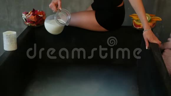 健身女孩把牛奶从玻璃杯倒入黑色浴缸热水视频的预览图