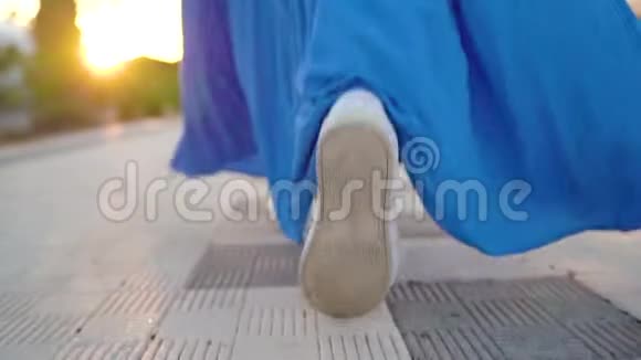 一个穿着漂亮蓝色裙子的女人在棕榈大道上行走的腿后景慢动作视频的预览图