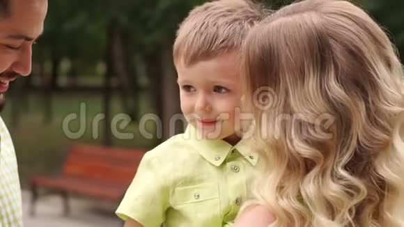 在公园里一个爱的爸爸妈妈的手里快乐的微笑着的小男孩视频的预览图