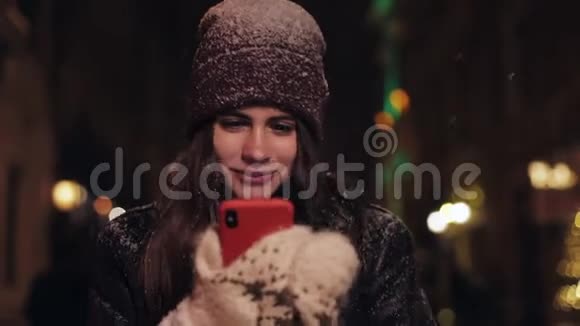 年轻女子带着智能手机在夜间行走的城市街道的肖像晚上在城市的智能手机上使用应用程序的女人视频的预览图