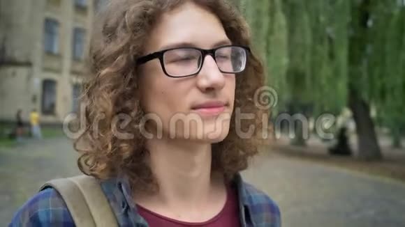 一位留着长长卷发的年轻学生点头向前看站在大学或校园附近的街道上视频的预览图