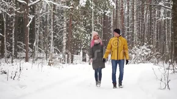 一个穿着黄色夹克的男人和一个戴着帽子和围巾的女孩在一场大雪中穿过冬天的森林笑着笑着视频的预览图