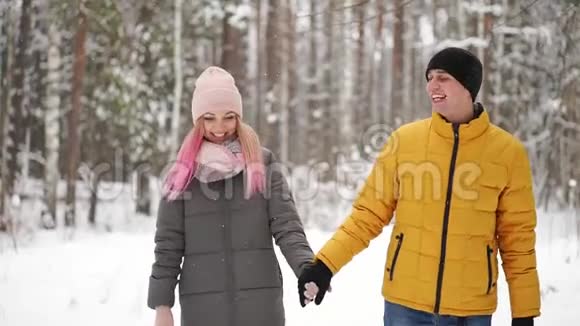 一个穿着黄色夹克的男人和一个戴着帽子和围巾的女孩在一场大雪中穿过冬天的森林笑着笑着视频的预览图