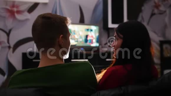 年轻可爱的一对夫妇坐在沙发上看电视拥抱视频的预览图