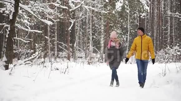一个穿着黄色夹克的男人和一个戴着帽子和围巾的女孩在一场大雪中穿过冬天的森林笑着笑着视频的预览图