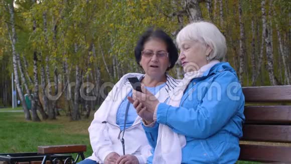 秋天的城市公园里两位老妇人在一起看手机视频的预览图