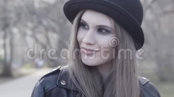 微笑迷人的时尚女孩与烟熏眼影戴黑色帽子和皮夹克行动小可爱视频的预览图