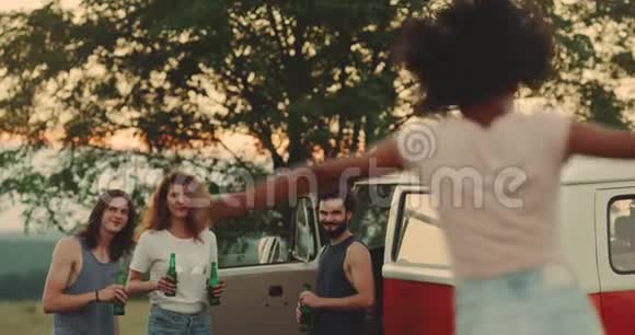 一群朋友带着他们复古的面包车在野地里野餐一边喝着啤酒一边微笑着度过美好的时光视频的预览图