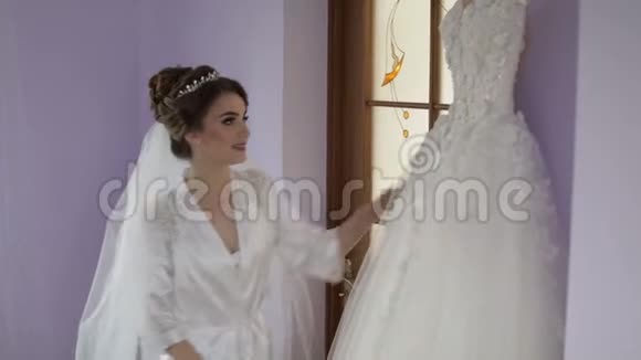 美丽可爱的新娘穿着睡衣站在婚纱附近结婚的早晨漂亮又整洁的女人慢动作视频的预览图