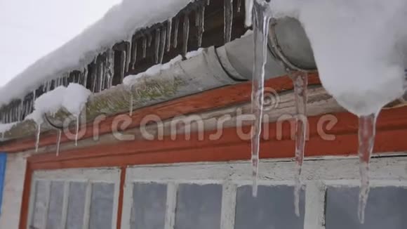 在冬天森林的某个地方挂在老房子屋顶上的长冰柱的特写镜头视频的预览图