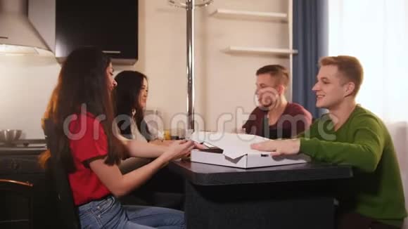 四个年轻的朋友坐在厨房里打开披萨盒视频的预览图