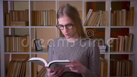 年轻漂亮的女学生戴着眼镜看着一本书微笑着看着镜头的特写照片视频的预览图