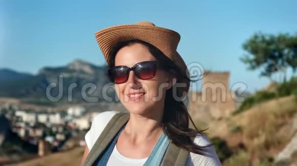 戴着帽子和太阳镜的微笑女游客在日落时度假的特写肖像视频的预览图