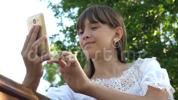 美丽的女孩在智能手机上写了一封春天夏天在公园的信一个年轻女孩在平板电脑上和朋友聊天视频的预览图